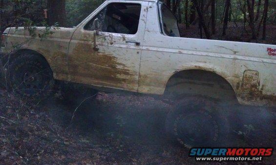 1990 Ford Bronco covered in mud, driving off-road