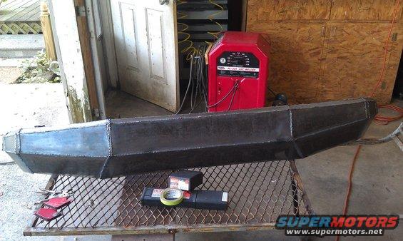 Custom fabricated steel bumper on a metal grate table with a red welding machine in the background