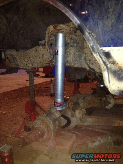 Close-up of a rusty vehicle axle and suspension parts supported by red jack stands, with a metal cylinder installed