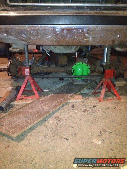 Vehicle undercarriage with front axle and differential visible, supported by jack stands
