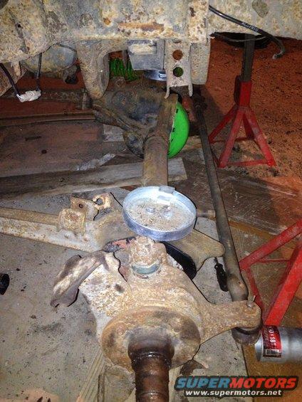 close-up of rusty vehicle suspension parts, including a ball joint and axle, with red jack stands visible