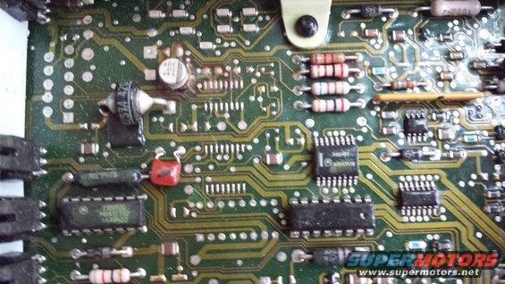 Close-up of a green circuit board with various resistors, capacitors, and integrated circuits. Text is visible on some components