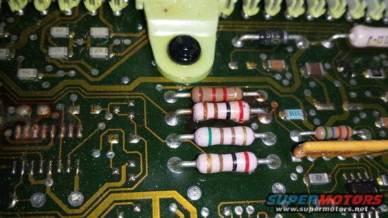 Close-up of a green circuit board with several resistors and electronic components. Some parts appear burnt