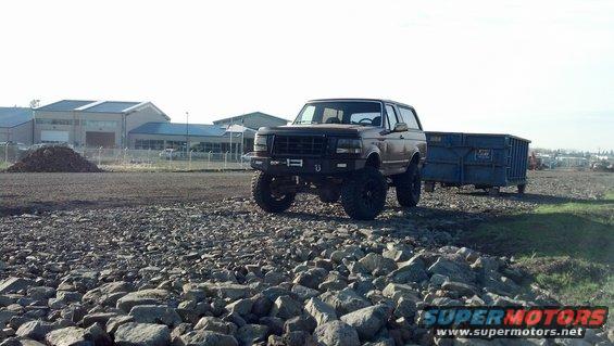 1992 Ford Bronco parked on rocky ground next to a blue dumpster trailer