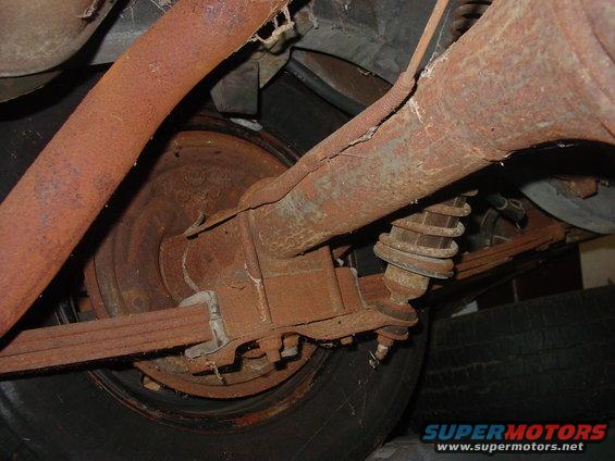 Rusty rear axle, leaf spring, shock absorber, and exhaust pipe under a vehicle