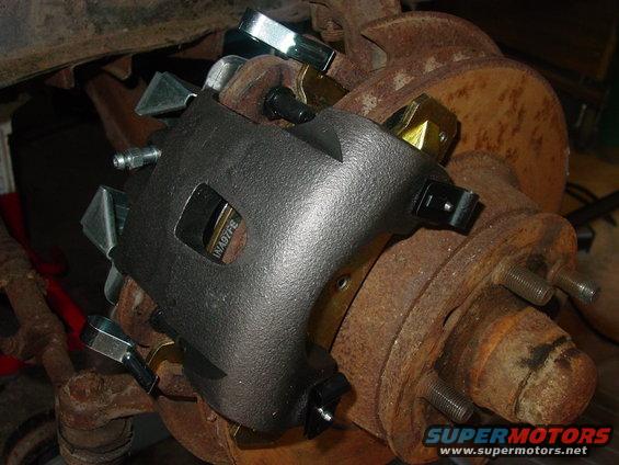 Black brake caliper with "INA97FE" visible, attached to a rusty rotor