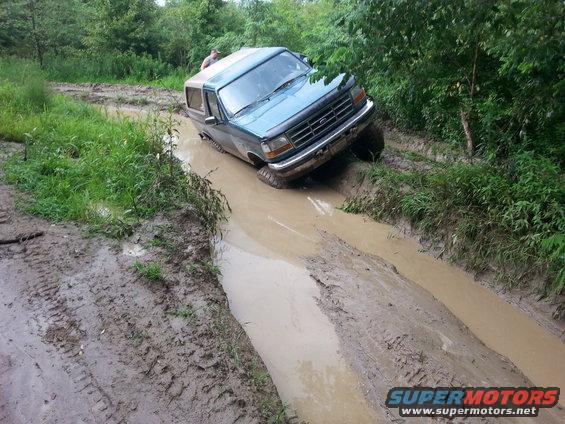 Ford Bronco stuck in a muddy ditch, driver visible in cabin