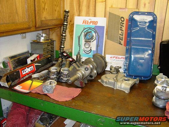 Crankshaft, camshaft, pistons, connecting rods, and Fel-Pro gasket sets laid out on a workbench