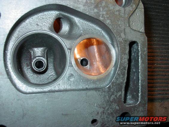 Engine cylinder head with two ports, one showing copper color