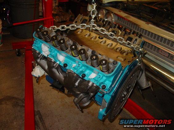 Engine being lifted by a chain hoist, with a car grille visible in the background