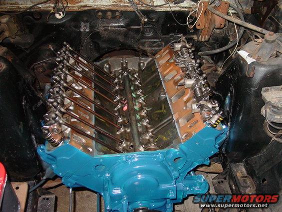 Blue V8 engine block with exposed valve train and oil pan, viewed from above