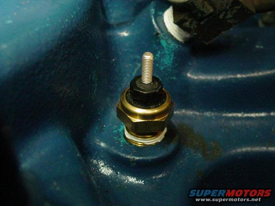 Close-up of an engine temperature sensor screwed into a blue engine block