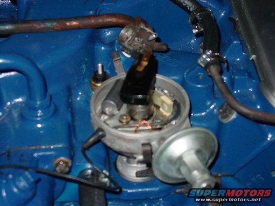 Close-up of an automotive ignition distributor with blue engine block in background