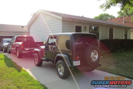 Dark green 2000 Jeep Wrangler, rear view, parked in driveway with trucks behind it
