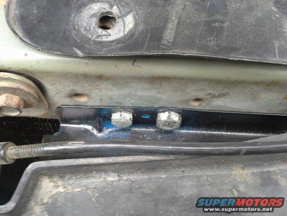 Close-up of a metal bracket with two bolts, part of a vehicle's engine bay