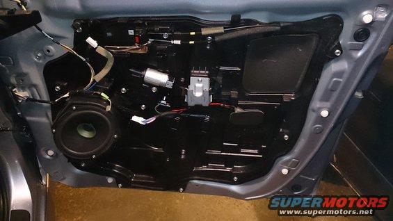 Car door interior panel removed, showing speaker, window motor, and wiring harness. Blue exterior paint visible