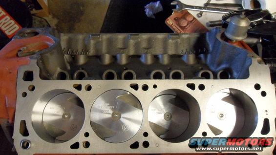 Engine block with pistons visible in cylinders. Some text is visible on the pistons and block
