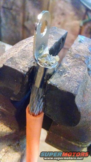 Battery cable terminal held in vise, with orange insulation visible