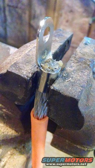 Corroded battery terminal clamp with frayed wires held in a vise