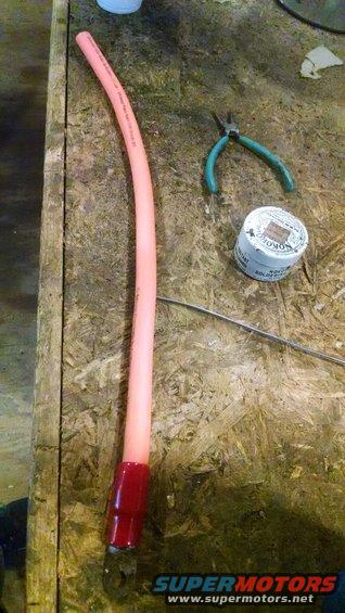 Pink hose with red fitting, pliers, and a spool of solder on a wooden surface