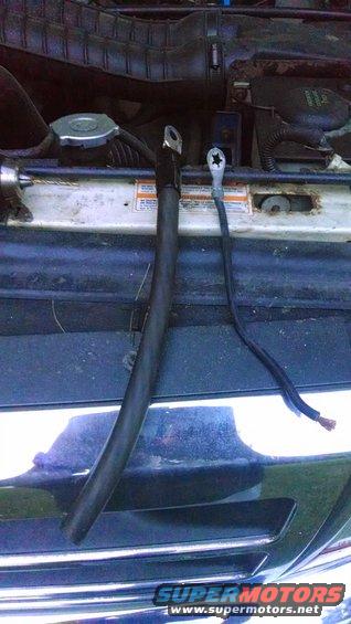 Engine bay showing two battery cables, one thick and one thin, with exposed wire ends on the thin cable