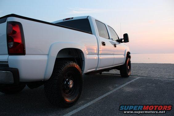 White pickup truck parked on pavement near the ocean at sunset
