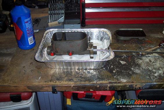 Brake master cylinder sitting in a foil pan with a bottle of brake fluid and tools nearby