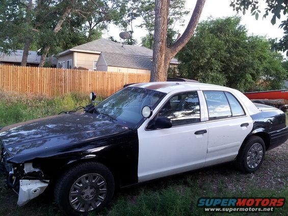Two-tone Ford Crown Victoria police car, front end is black, rear is white. Missing front bumper