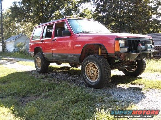 Red Jeep Cherokee XJ with aftermarket bumper and winch parked on gravel and grass