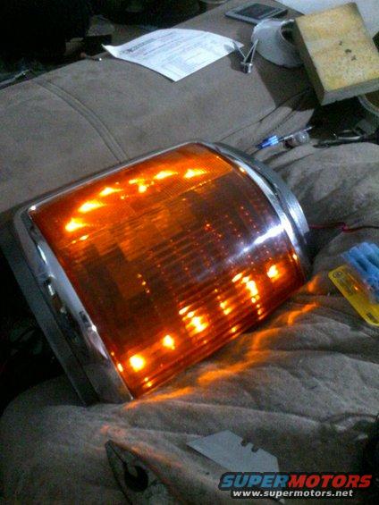 Orange turn signal assembly with chrome trim, lights on. Sitting on a blanket