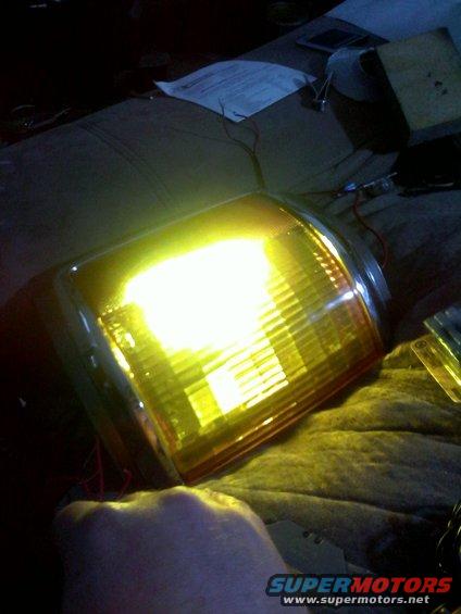 Yellow turn signal assembly with chrome trim, wires attached, on a textured surface