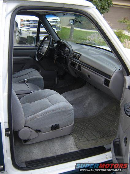 Interior view of a white 1992 Ford Bronco, showing front seats and dashboard. Another white truck is visible through the windshield