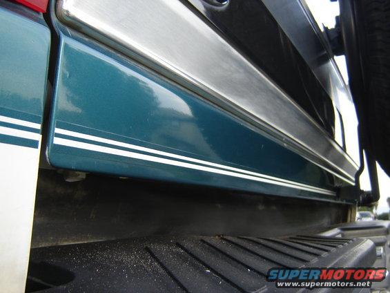 Close-up of teal vehicle side panel with silver trim and white pinstripes. Spare tire visible on right