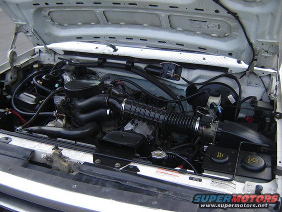 engine bay with hoses, air intake, and various engine components visible