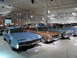 1971 Ford Ranchero - Several classic cars are on display in a museum, including a light blue coupe and a tan coupe.