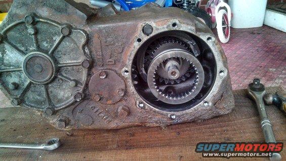 close-up of a rusty transfer case with gears visible inside, tools on the side