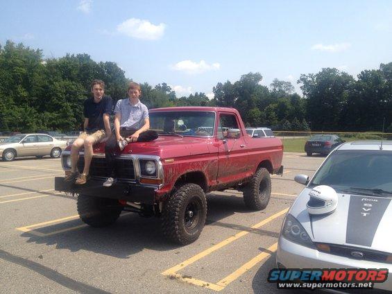 Red 1978 Ford Bronco with two people on hood, lifted suspension, off-road tires