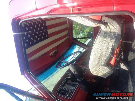 Interior view of a red truck cab showing a steering wheel, dashboard, and an American flag sunshade