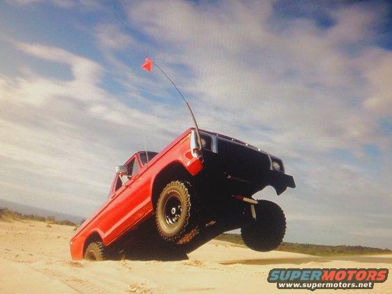 1978 Ford Bronco driving on sand dunes with a red flag on an antenna