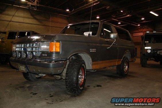 Gray Ford Bronco with wood paneling on the side, parked indoors next to another SUV