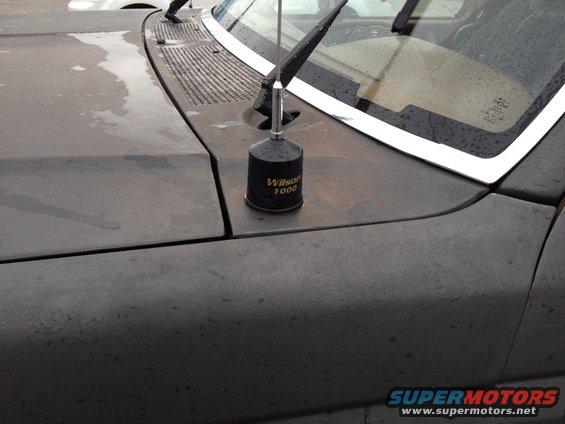 Close-up of a dark-colored car hood showing a Wilson 1000 antenna and part of the windshield