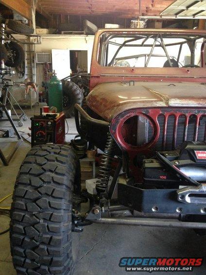 Red Jeep CJ-series front quarter view with large off-road tires and roll cage