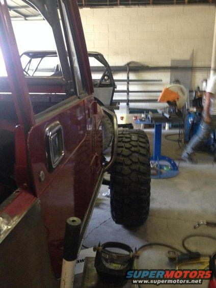 Side view of a red Jeep CJ-series with large tires, another Jeep tub visible behind it in a workshop