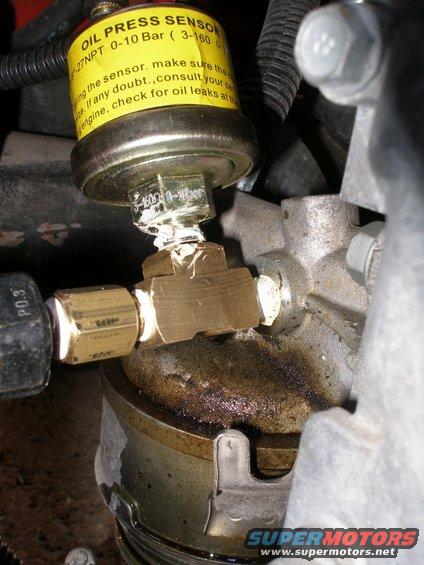 Yellow oil pressure sensor with black text, connected to a brass T-fitting