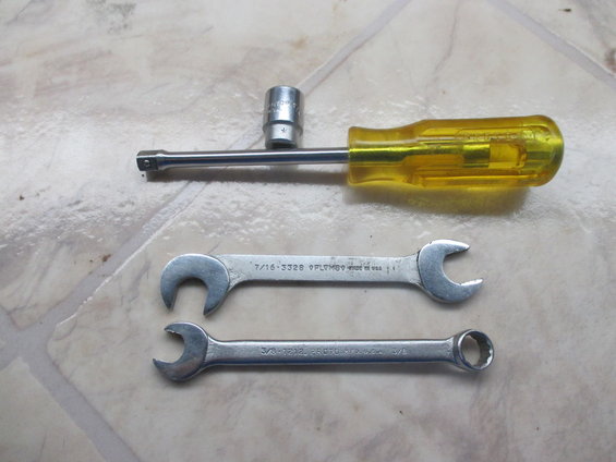 Two wrenches and a socket wrench with a yellow handle on a tiled surface