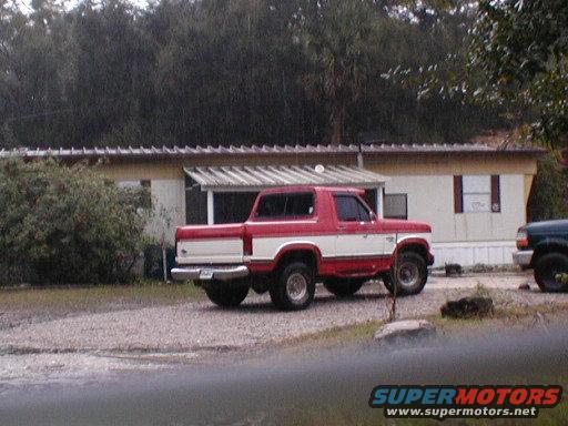 Red and white Ford Bronco parked in front of a mobile home, with another dark SUV to the right
