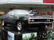 1979 Ford Bronco II - A black 1970 Dodge Charger with a prominent hood scoop is displayed on a raised platform in front of a building.