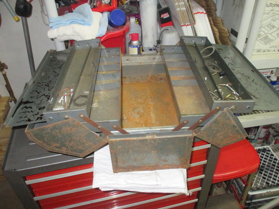 open metal toolbox with compartments, some rust, sitting on a red tool chest