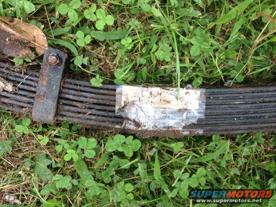 Leaf spring with tape and a bolt on grass. Supermotors.net logo visible