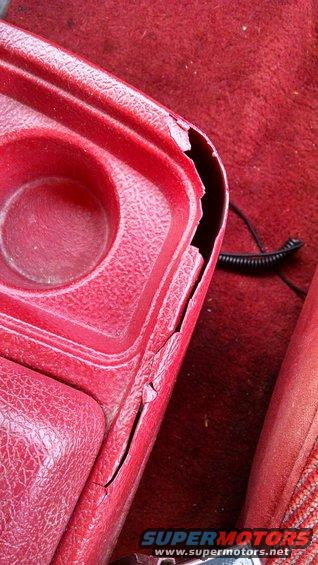 Close-up of a cracked red plastic console with a cup holder and a coiled black wire on red carpet
